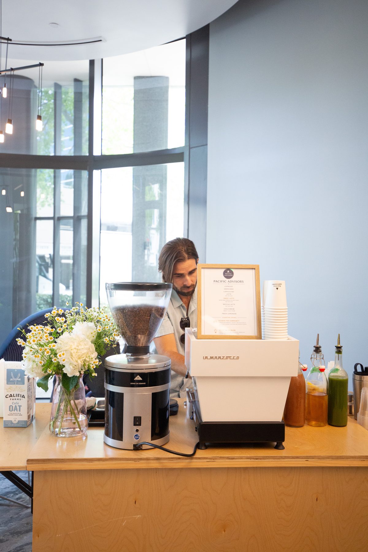 Barista working behind the birch coffee cart with fresh flowers and a white espresso machine