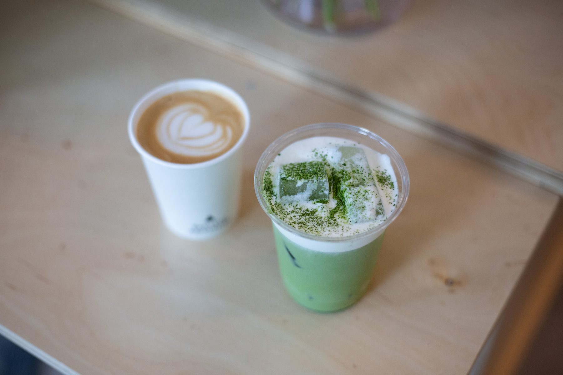 A hot latte and an iced matcha latte side by side on the cart